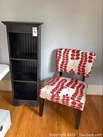 Photo showing the black shelving unit with three shelves and the upholstered side chair with red leaf patterned fabric and black legs side-by-side.