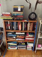 Photo of a wooden bookshelf with four shelves filled with various books in different sizes and colors, including some stacked horizontally.