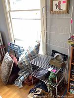 View of multiple pillows, blankets, white wire racks, and several purses on the floor and racks.