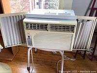 Daewoo window air conditioner with side panels open, shows weathered condition and mounted on a stand indoors.