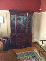 Full view of dark wood china cabinet with glass front doors and drawers below, standing in a room with paneled walls and hardwood floor.