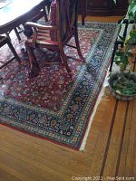 Lower corner of rug showing red field, turquoise and navy floral border, ivory fringe and sun-faded area