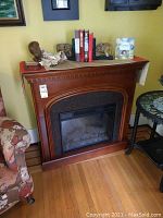 Front and side angled view of electric fireplace with wooden mantel showing overall design and scale compared to nearby furniture.