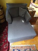 Front view of one light blue/grey chaise lounge chair with two matching cushions on a wooden floor with area rugs nearby.