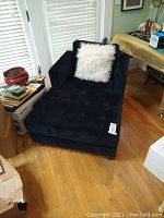 Dark blue chaise lounge chair with white fluffy throw pillow seen from side near window with hardwood floor