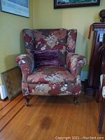 Front angle of the floral wingback chair with a purple pillow.