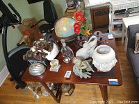 View of tabletop with globe, ceramic vases, glassware, silverplate and figurines