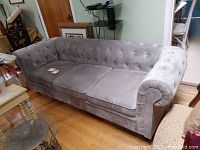 Full view of the gray microfiber sofa showing tufted back and rolled arms with wood legs on a hardwood floor.
