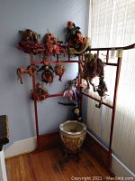 Two-piece wooden coat rack corner setup with metal hooks along upper edges holding several holiday-themed decorative art dolls and a marionette horse. A decorative vase is placed below but not included.