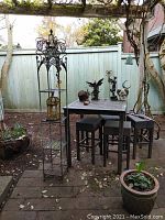 Overall view of gray outdoor dinette table, four stools and tall metal etagere shelf under pergola