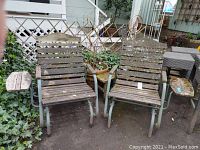 Two wooden slat chairs on gray metal frames with built-in side trays, showing weathering and moss.