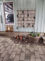 Wide view of yard area showing gargoyle and cherub figurines, large wooden planter, ceramic pots and wooden lattice with string lights and grape decor on wall