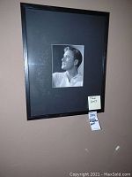 Framed black and white actor portrait print on hanging wall with two tags visible.