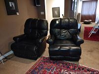 View of two black leather recliners side by side on a carpet with pillows and walls in background