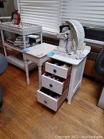 Two white side tables, one with three drawers open, visible wear and items inside drawers, white angel figurine on top.
