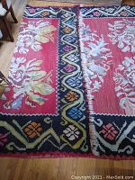 Photo of the entire wool kilim rug laid out flat on hardwood floor showing floral motifs, colorful black border, and frayed edges.