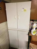 Front view of two stacked white cabinets with four doors and two drawers in an indoor environment, showing signs of use including marks and scratches.