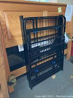 Folded black metal bed frame leaning against the oak headboard.