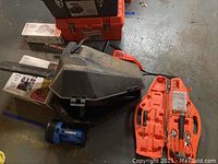 Overall view of various tools including tool boxes, chainsaw parts, and power tools on floor.