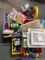 Overview photo showing multiple crates containing electrical cords, switches, heat register covers, painting kit, and other home maintenance items.