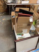 Cardboard boxes containing assorted picture frames stacked together, some frames leaning outside boxes