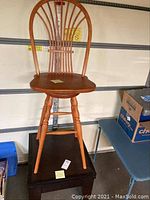 Full view of the Windsor style wooden bar stool showing curved spindle backrest and turned legs, placed on a dark wood table.