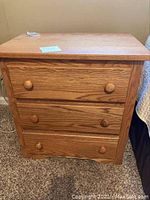 Front view of the oak chest showing three drawers with wooden knobs and natural oak grain.