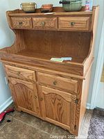 Full view of the oak dry sink showing three top drawers, an open shelf, and lower cabinet doors with knobs.