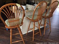 Three oak swivel barstools with high spindle backs and cushioned seats positioned at kitchen counter