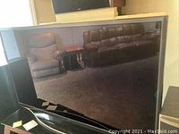 Front view of large black Samsung television, reflective plasma screen showing the room behind.