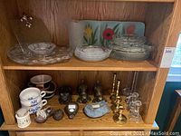 Shelf with clear and frosted glass serving dishes, mugs, animal doorstops, and candlestick holders
