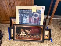 Two framed wall art pieces displayed on floor, one with dog image and the other with cat/artistic design