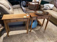 Overview of two oak console tables side by side on carpeted floor