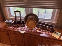 View of the full set of items on window ledge including the two metallic bowls with stands, the cast iron jug/pot, the wooden wine carrier, decorative runner beneath, and planter box.