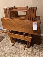Four folded oak TV trays stored vertically in an oak tray stand showing wood grain and structure