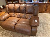 Front view of the two-seat brown leather reclining sofa showing padded cushions and armrests, with visible wear.