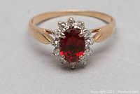 Front angle of ring showing oval red garnet center and surrounding diamonds