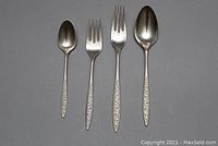 Four flatware pieces laid out side by side on a grey background showing overall set composition and pattern continuity.