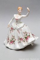 Front view of Royal Doulton Shirley figurine showing floral patterned dress and raised right arm.