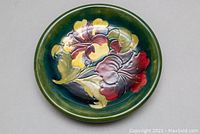 Top-down view of the round Moorcroft plate showing the floral design and green background.