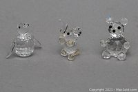 Front view of three Swarovski crystal figurines: penguin, elephant, teddy bear against grey background