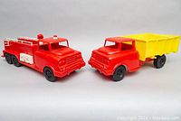 Side view of the red fire truck and red/yellow dump truck showing both trucks from the side.