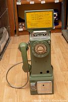 Front view of green rotary pay phone showing dial, coin slots, instruction panel