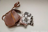 Bolex Paillard 8mm film camera partially in brown leather case, showing camera body with three lenses and dials.