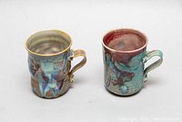 Front view of both pottery mugs showing multicolor glazing and handles