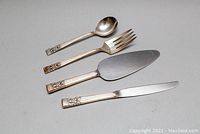 Four flatware pieces including a teaspoon, dinner fork, pie server, and dinner knife showing ornate handles