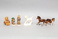Overall view of all six figurines showing white horse, brown horse, Royal Doulton collie, and three child figurines