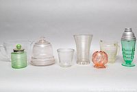 Full view of all 8 Depression glass items arranged in a row showing variety of colors and styles.