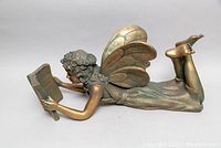 Side view of large carved wooden angel sculpture lying prone reading a book with legs bent upward.