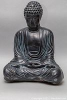 Frontal close-up of Buddha sculpture showing seated meditative pose and detailing on robes and hair curls.